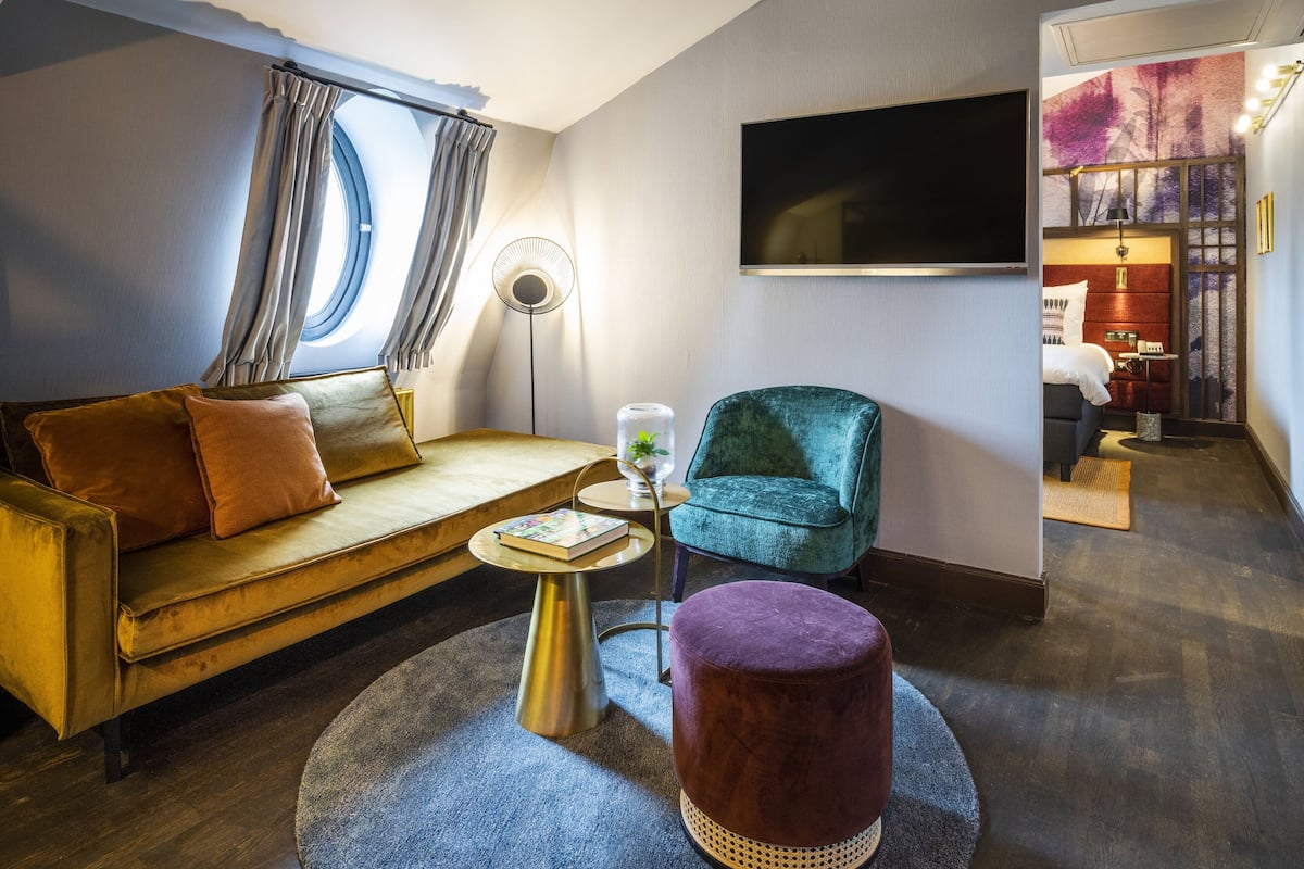 A modern living room with a sofa, a round coffee table, a teal armchair, and a purple ottoman.