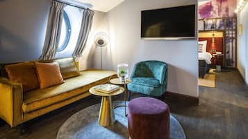 Una sala moderna con un sofá, una mesita redonda, un sillón color esmeralda y un otoman púrpura.