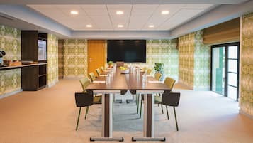 A conference room with a long table, chairs, a TV screen, and a small bar area with a plant.