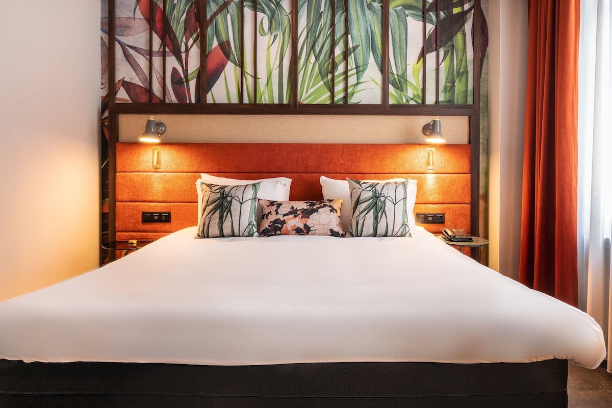 A hotel room with a large bed, two bedside tables, a wall-mounted lamp, and a decorative plant wall.