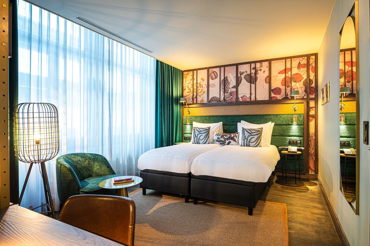 A hotel room with a large bed, a chair, a small table, and a lamp.