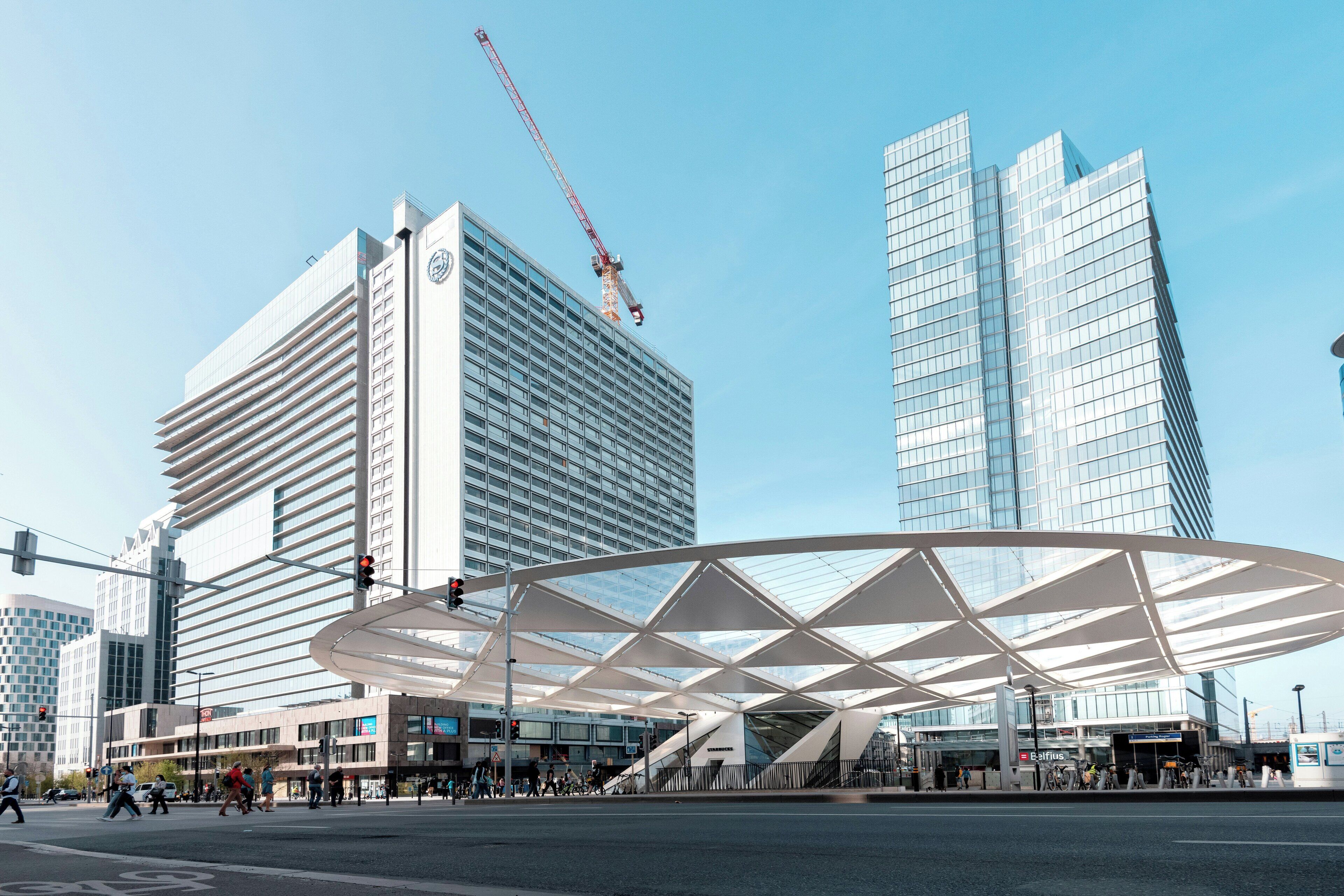 A modern urban intersection with contemporary buildings, a pedestrian crossing, and a distinctive white canopy structure.