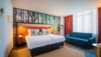 Quarto de hotel com uma cama grande, um sofá azul e uma mesa pequena.