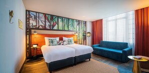 A hotel room with a large bed, a blue sofa, and a small table.