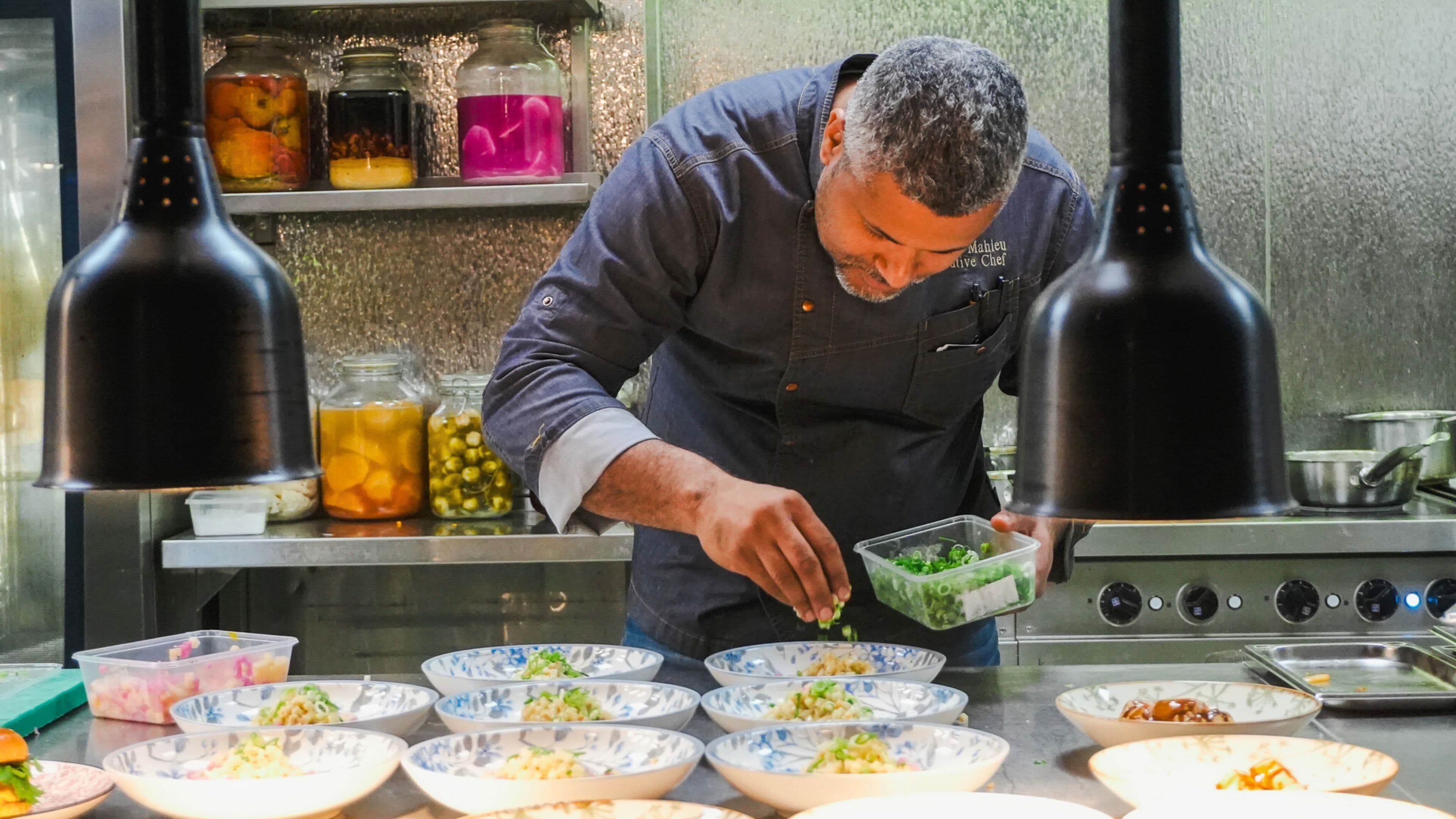 Un chef preparando comida en una cocina con varios recipientes de ingredientes y una estufa.