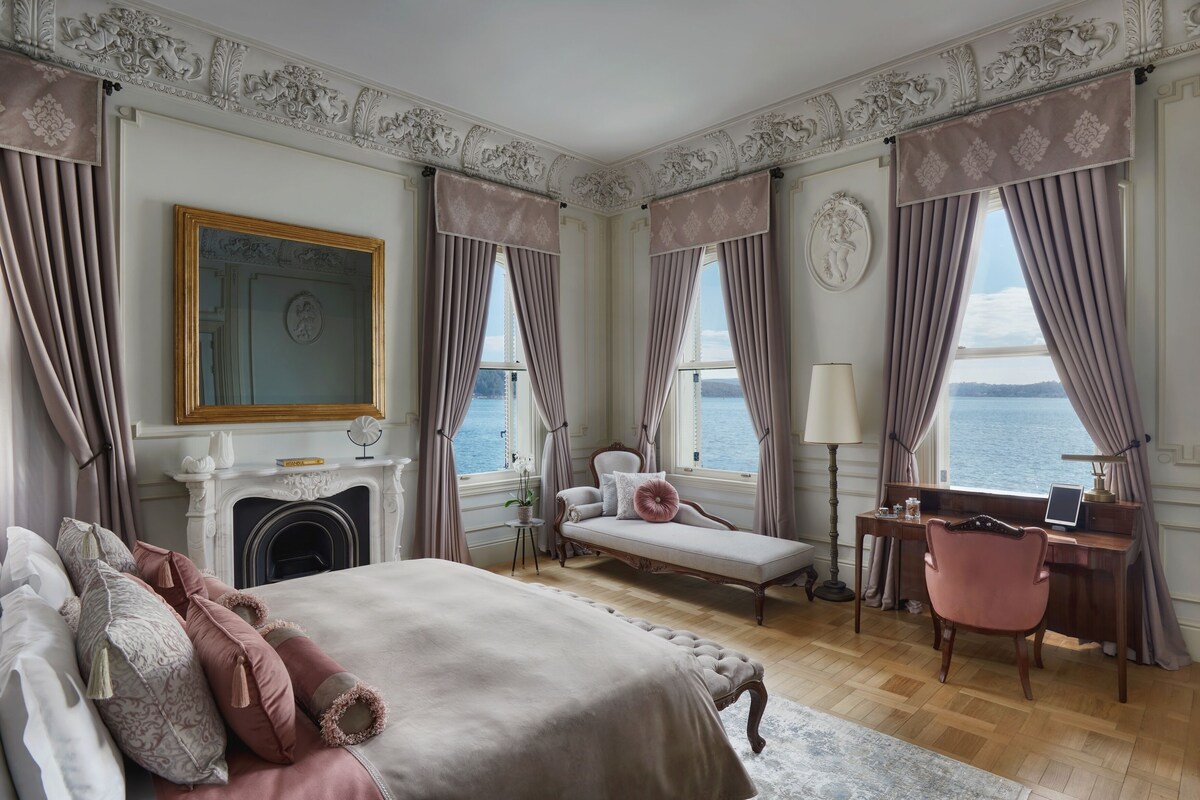 A bedroom with a bed, a sofa, a desk, and a view of the sea.
