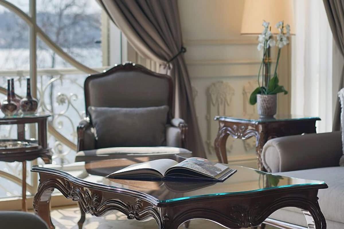 A room with a glass-top table, a chair, a sofa, a lamp, and a window with curtains.