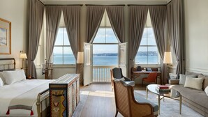 Quarto de hotel com cama, escrivaninha, poltrona e vista para o mar.
