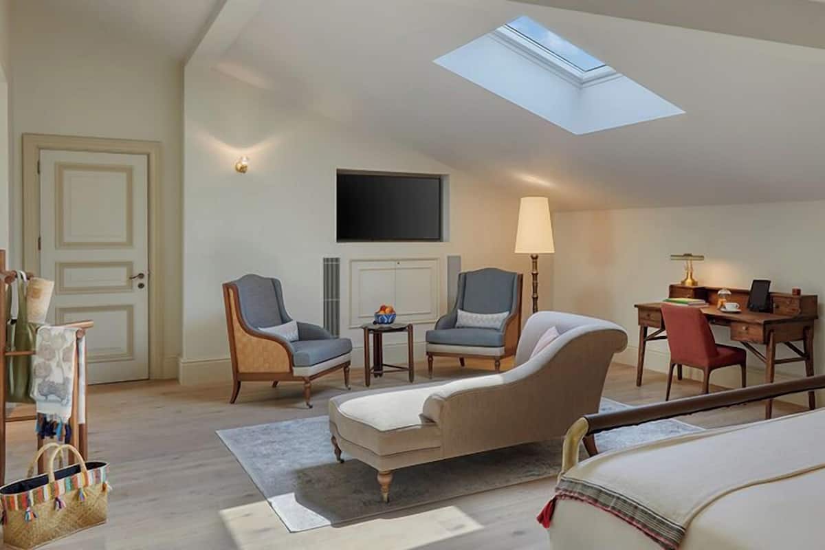 A room with a skylight, two armchairs, a sofa, a desk with a chair, and a bed.
