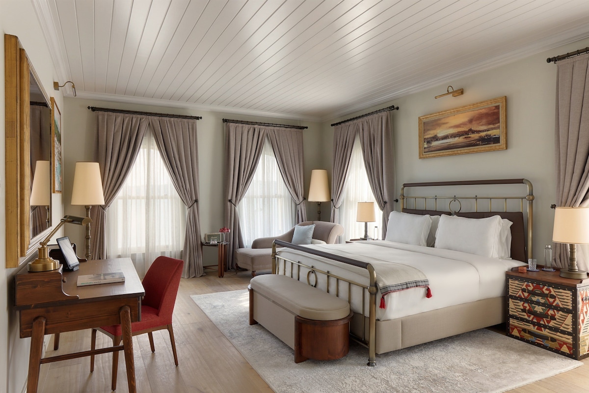 A hotel room with a large bed, a desk, a chair, a bench, and a nightstand.
