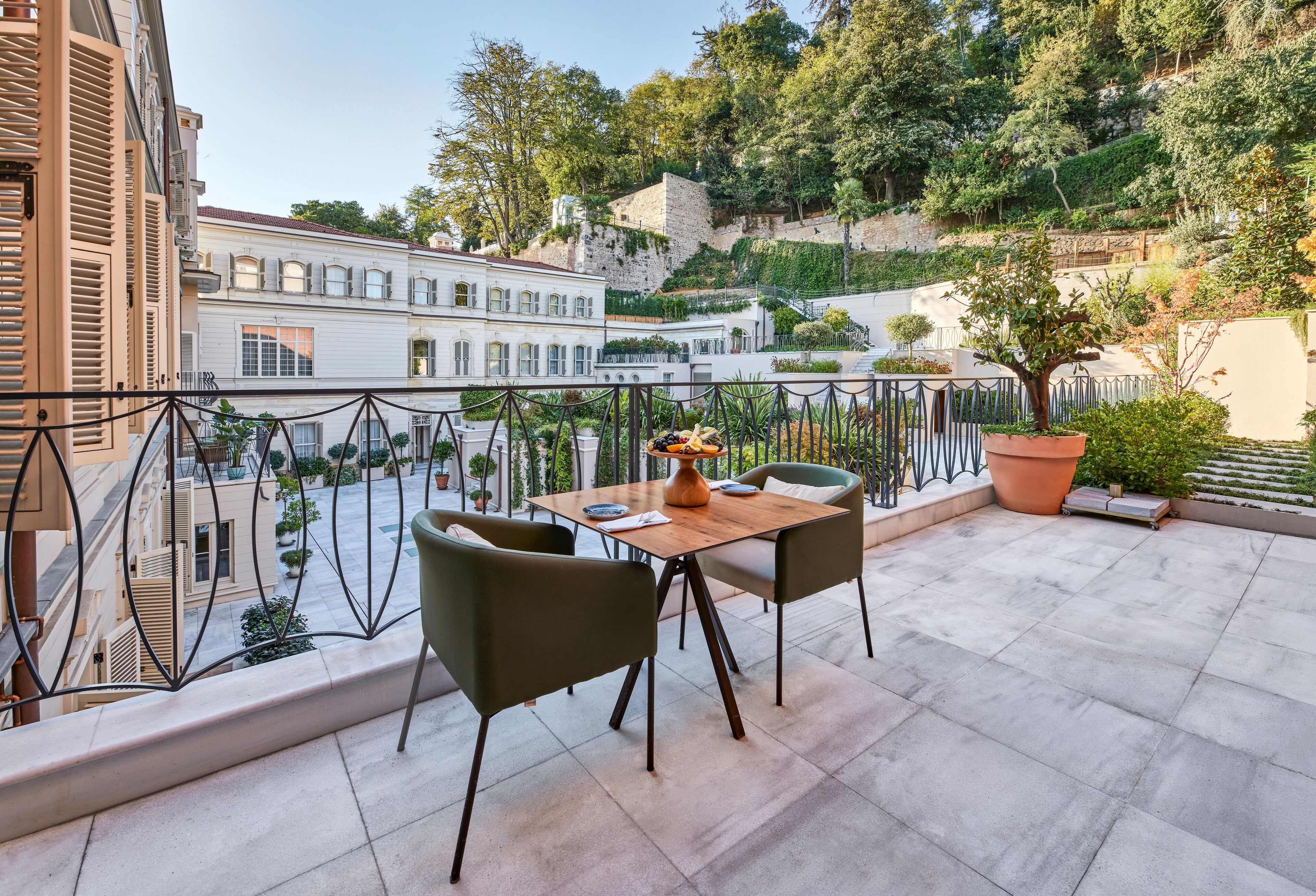 A terrace with a table and chairs, overlooking a courtyard with buildings and trees.