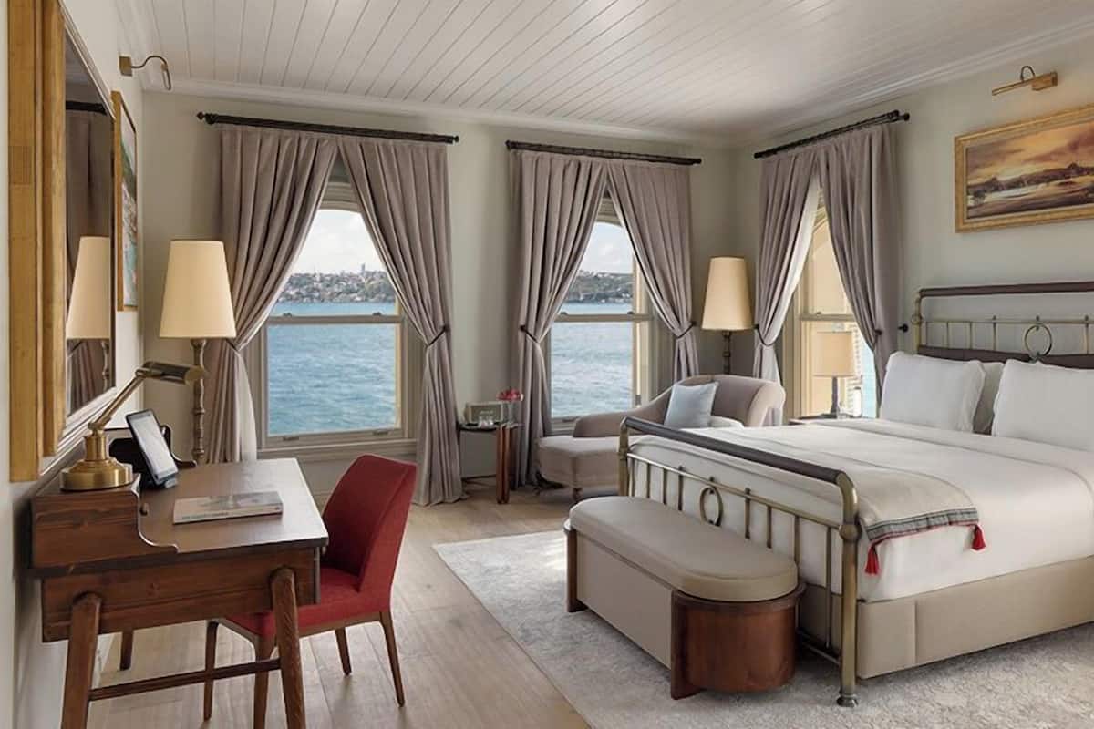 A hotel room with a bed, desk, chair, and a view of the sea.