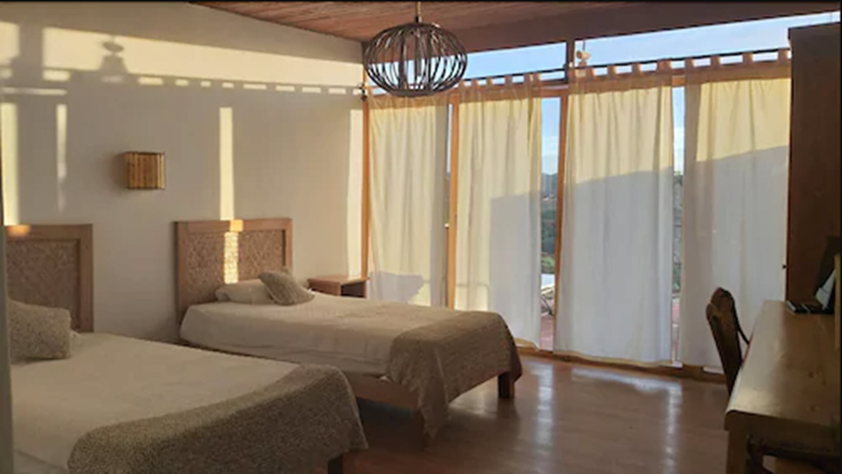 Un dormitorio con dos camas, techo de madera y un ventanal con cortinas.