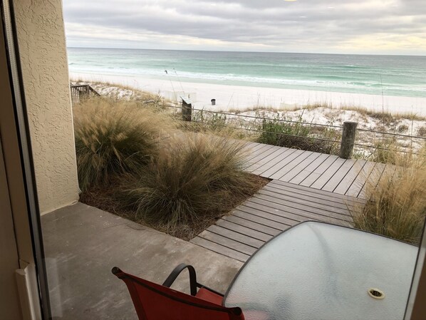 Uitzicht vanaf een balkon op een strand met een houten terras en een glazen tafel.