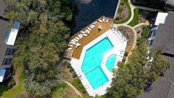 Vue aérienne d’une propriété dotée d’une piscine, d’une terrasse avec des chaises longues et d’un espace verdoyant environnant.