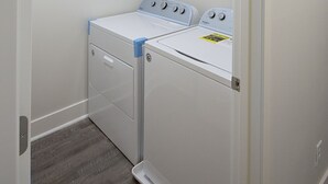 Un lavadero con dos lavadoras y secadoras blancas, suelo de madera y una puerta blanca.