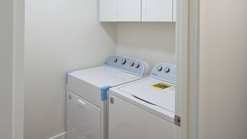 Une buanderie avec deux machines à laver et deux sèche-linge blancs, un plancher en bois et une porte blanche.