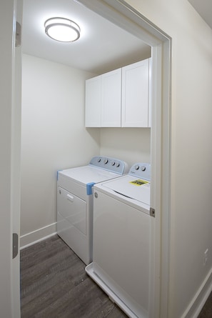 A laundry room with two white washers and dryers, a wooden floor, and a white door. - HIDEAWAY VILLA: Walk to Beach & Coligny,Pool, Fireplace, 3BR/3.5 BA (Hilton Head Island)