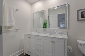 A modern bathroom with white cabinetry, a marble countertop, two mirrors, and a toilet.