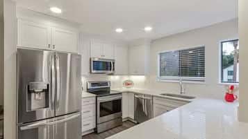 A modern kitchen with stainless steel appliances, white cabinetry, and a large window.