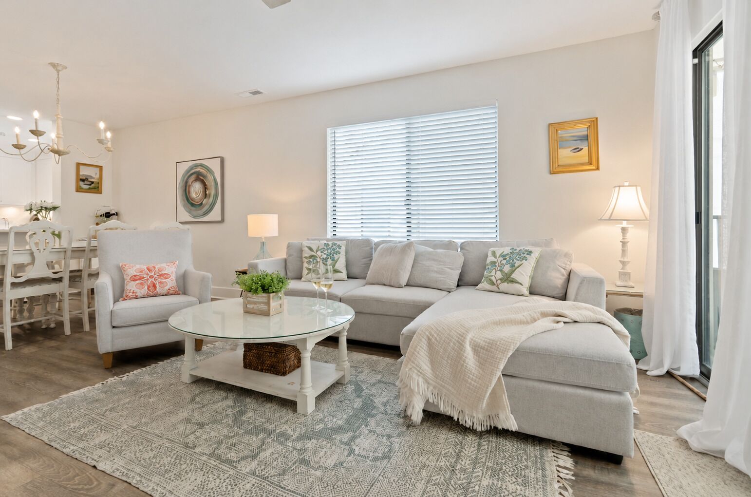 A modern living room with a glass coffee table, grey sofa, and a dining area with white chairs.