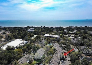An aerial view of a residential area with houses, a large building, and a body of water in the background.