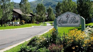 A sign for 'Quail Run' with a view of a residential area and a mountain in the background. - Quail Run - 3367 (Steamboat Springs)