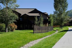 Une maison à deux étages, dotée d’un toit en pente, entourée d’une clôture en bois et bordée d’un chemin de gravier menant à l’allée.
