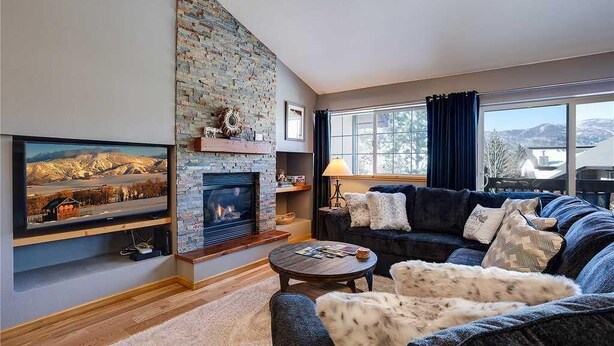 A cozy living room with a fireplace, a large TV, a comfortable sofa, and a view of the outdoors. - Quail Run - 3367 (Steamboat Springs)