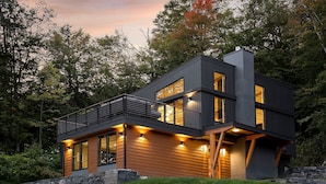 A modern two-story house with a balcony, large windows, and a stone foundation.