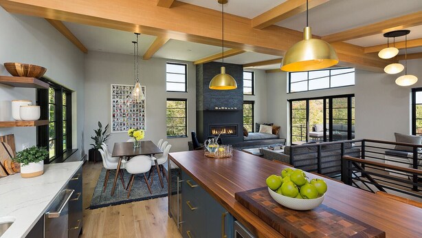 A modern kitchen with a central island, wooden beams, pendant lighting, and a fireplace.