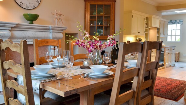 A dining room with a wooden table set for a meal, a wall clock, and a vase with flowers. - 3 bedroom accommodation in Keswick (Keswick)