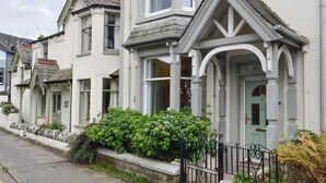 A row of white houses with green accents, a stone wall, and a black metal fence. - 3 bedroom accommodation in Keswick (Keswick)
