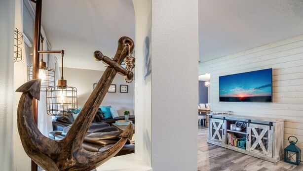 Ein Wohnzimmer mit einer großen Anker-Skulptur, einem Holztisch und einem an der Wand befestigten Fernseher.