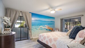 Ein Schlafzimmer mit Strandwandgemälde, Deckenventilator und einem großen Bett mit gemusterten Betttextilien.