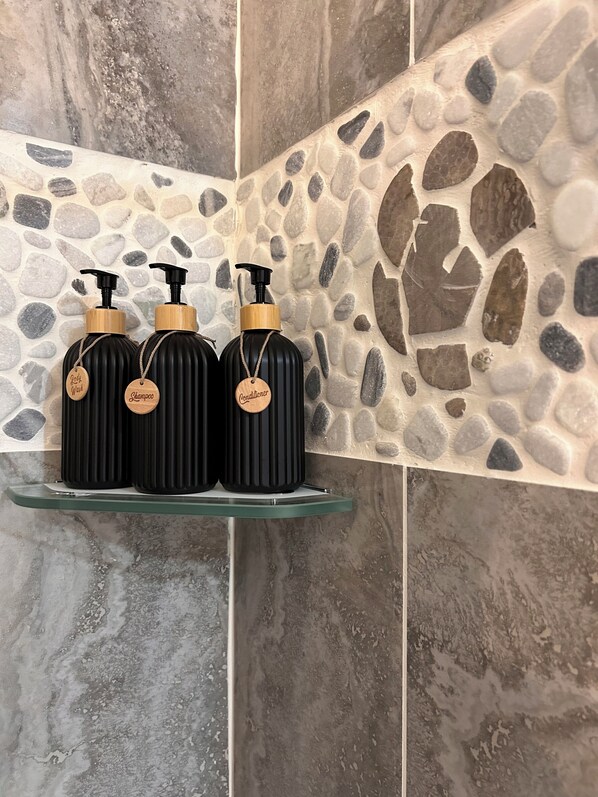 Three black bottles with wooden caps and tags on a glass shelf against a stone wall.