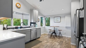 A modern kitchen with grey cabinets, a dishwasher, a refrigerator, and a dining area with stools. - Pet friendly, waterfront, home on Lake Leelanau. Pontoon available for rent (Lake Leelanau)