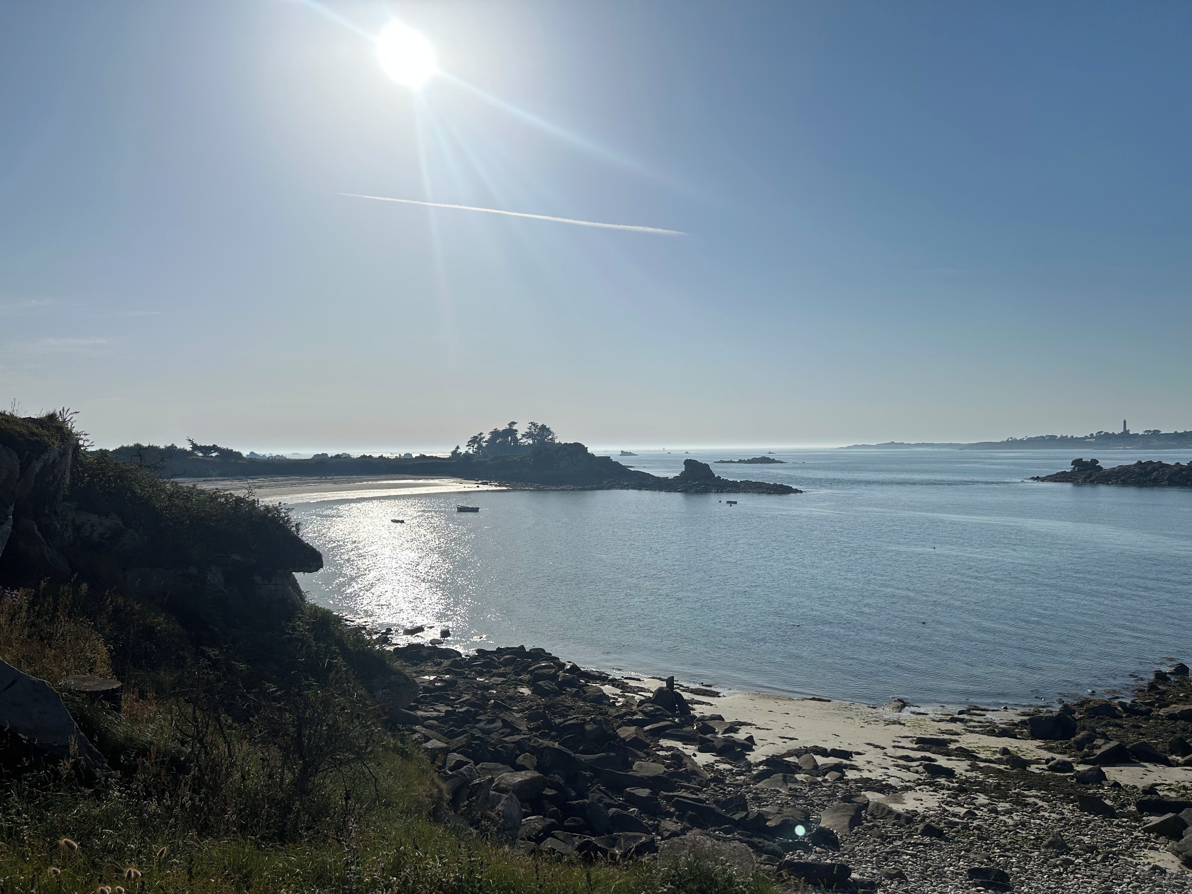 A coastal landscape with a rocky shoreline, calm water, and distant landforms.