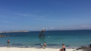 Een strand met helderblauw water, een uitkijktoren van de badwachter en een rotsachtige kustlijn.
