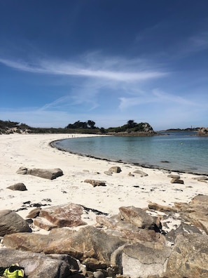 Una playa con grandes rocas en primer plano y un cielo despejado.