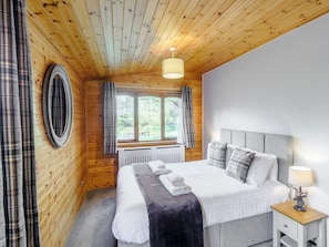 A wooden-paneled room with a bed, a window, a radiator, and a nightstand with a lamp.