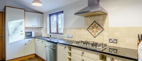 A modern kitchen with white cabinets, a stainless steel dishwasher, a gas stove, and a window with a view of the outdoors.
