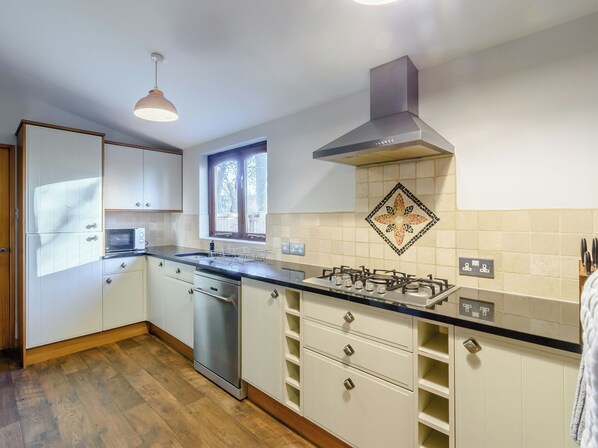 A modern kitchen with white cabinets, a stainless steel dishwasher, a gas stove, and a window with a view of the outdoors.