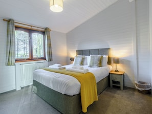 Une chambre à coucher bien rangée, avec un lit, des tables de chevet et une fenêtre avec des rideaux.