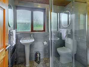 A modern bathroom with a glass-enclosed shower, a pedestal sink, and a toilet.