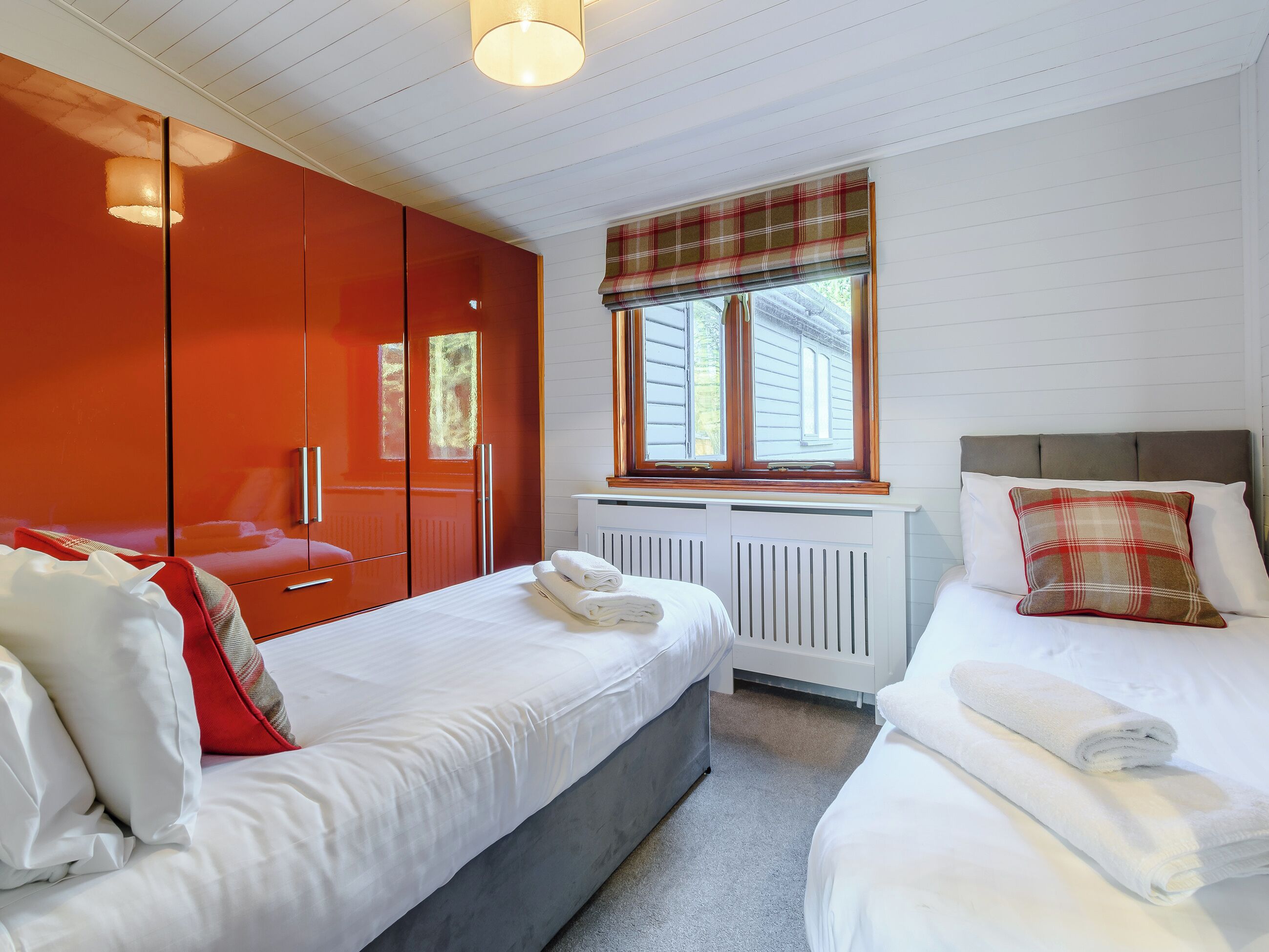 A bedroom with two beds, a wardrobe, a window with a plaid blind, and a radiator.