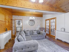 Un salon chaleureux avec un canapé d’angle gris, un fauteuil à motifs écossais et un plafond en bois.