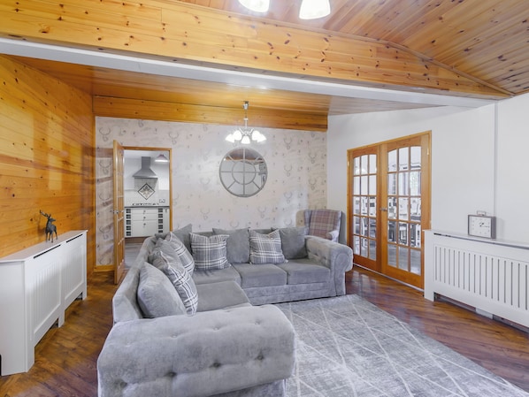 A cozy living room with a grey sectional sofa, a plaid armchair, and a wooden ceiling.