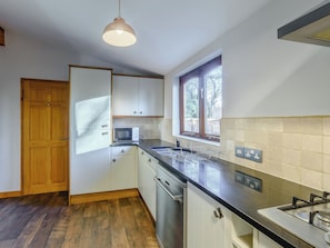 Une cuisine moderne avec des meubles blancs, une porte en bois, un four à micro-ondes, un évier et une fenêtre donnant sur des arbres.