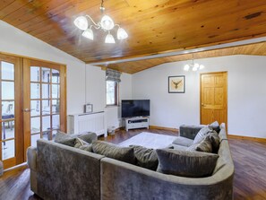 A living room with a wooden ceiling, a grey sofa, a TV, and a door. - 4 bedroom accommodation in Cayton, near Scarborough (Cayton, near Scarborough)